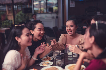 A group of female friends laugh and point at each other as they reminisce the good old days over a delicious dinner at an al fresco restaurant. Night life with friends.