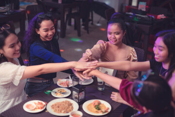 Fototapeta na wymiar Five young women putting their hands together at the center of the table doing a friendship huddle and making a promise. Workmates piles their hands up each other showing team spirit and unity