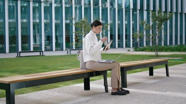 Student taking coffee break from online studying sitting bench near building.
