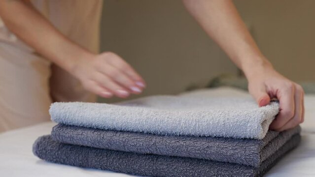 Close-up of hands putting a stack of fresh bath towels on a sheet. Room service maid cleaning the hotel room