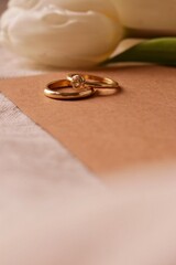 Dwie złote obrączki leżą razem na kartce. Ciepła stylistyka na zaproszenie ślubne lub...
