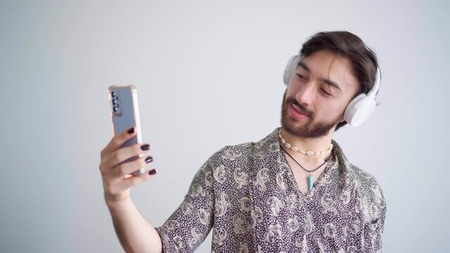 Young queer latin gay man taking pictures of himself with a headphone on a white background. 4k video.