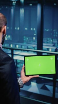 Vertical video: Support specialist using tablet with greenscreen display in modern data center, checking blank chroma key template. Database admin working with isolated mockup and hardware industry