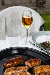 Hot grilled sausages, wine in a glass, mineral water, and plates on the table during dinner. Selective focus.