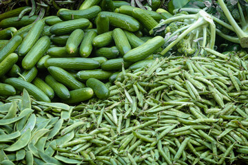 Heap of green vegetables like cucumber, broccoli, green peas and broad beans in a vendor cart