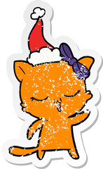 distressed sticker cartoon of a cat with bow on head wearing santa hat
