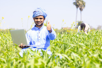 Asian Indian young farmer businessman holding laptop showing thumb up after crops examine