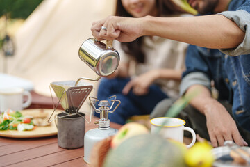 Asian couple drip coffee in the camp enjoying camping outdoors in nature. Man traveler hands holding cup of coffee.