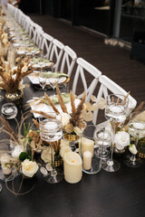 Wedding decorations. Served wedding table with white chairs golden plates, green napkins, decorative fresh and dried flowers, candles and and light bulbs. Celebration details, wedding outdoor
