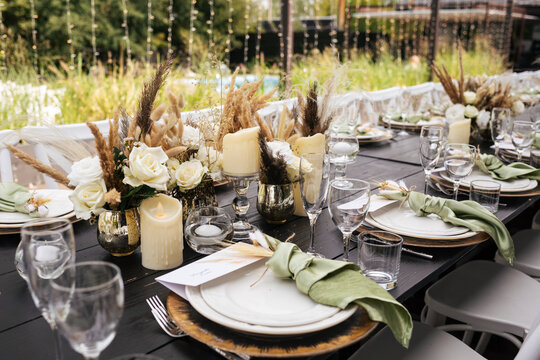 Wedding decorations. Served wedding table with golden plates, green napkins, decorative fresh and dried flowers, candles and and light bulbs. Celebration details, wedding outdoor