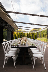 Wedding decorations. Served wedding table with white chairs golden plates, green napkins, decorative fresh and dried flowers, candles and and light bulbs. Celebration details, wedding outdoor

