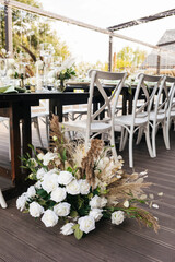 Wedding decorations. Served wedding table with white chairs golden plates, green napkins, decorative fresh and dried flowers, candles and and light bulbs. Celebration details, wedding outdoor
