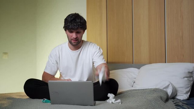 Man who feels sick, sitting at home on a bed, drips nasal drops into a stuffy nose. A man sprays cold medicine for a runny nose and listens to the doctor using a laptop.