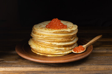 Pancakes with red caviar. A pile of pancakes. Pancakes on a plate and with caviar on a wooden spoon. Red caviar.