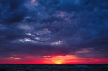 Naklejka na ściany i meble Dramatic sunrise over ocean. Red and dark clouds over sea. Sunrise or sunset.