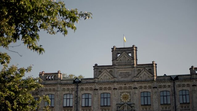 The flag of Ukraine grows on the roof of the ancient building. The facade of the Kyiv Polytechnic Institute with ukrainian flags in the front.