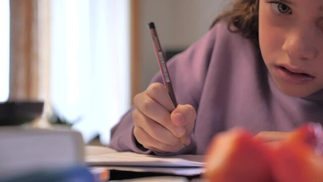 Close-up of girl eating fruits while doing homework at home