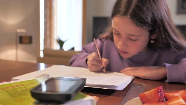 Girl doing homework with glucose meter and strawberries on top of a table