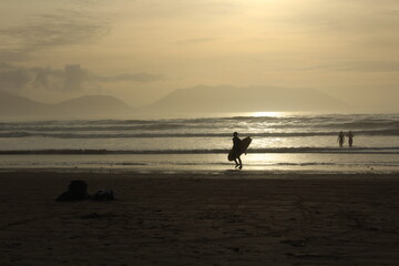 Silhouette of a person surfing at Inch beach at sunset with swimmers in the water (Dingle Peninsula, County Kerry, Ireland).Concept for cold water swimming in winter