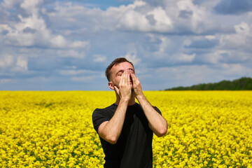 man in field blowing his nose and suffering from hay fever.