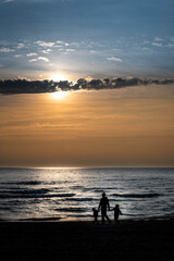 A family of three (parent with 2 children) walking by the sea during a very beautiful yellow sunset
