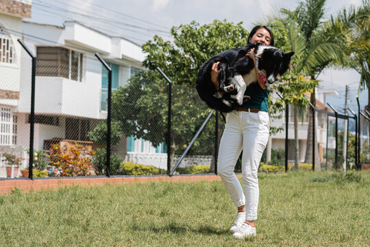 Positive young ethnic lady hugging cute dog in park