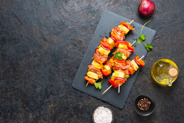 Raw prepared skewers with chicken, pineapple and sweet peppers on a black slate board against a black concrete background. Step by step recipes, cooking.