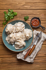 Georgian dumplings Khinkali on plate with red tomato sauce and fresh cilantro top view on rustic wooden background, traditional dish of Georgia