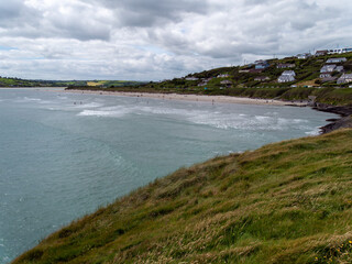 View of Inchydoney beach from the Cape of the Virgin Mary. Irish seascape. A European settlement on the shore. Green grass near body of water, cloudy sky