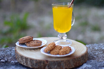 Glass of orange juice with reusable straw and two plates with cookies, served in a garden. Selective focus.