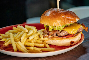 a close up image of a Guacamole and bacon filled beef burger served with French fries 