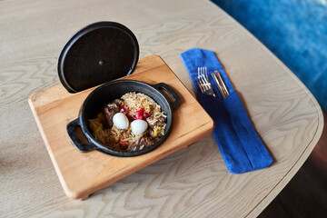 Pilaf on a platter with beef on a wooden background with appliances. The concept of Oriental cuisine. Homemade Uzbek beef pilaf is served in cast-iron dishes. Space for copying. High quality photo