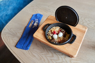 Pilaf on a platter with beef on a wooden background with appliances. The concept of Oriental cuisine. Homemade Uzbek beef pilaf is served in cast-iron dishes. Space for copying. High quality photo