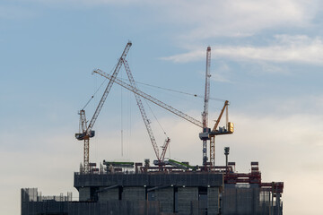 Obraz premium Close-up industrial big cranes working on construction site to build modern tall buildings on evening, growth in the city