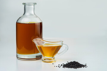 A handful of black cumin seeds on the background of a glass gravy boat nd a bottle with black seed...