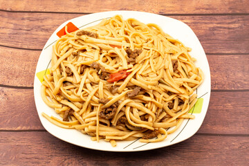 Salted noodles with vegetables, onion and pieces of beef garnished on a white plate on a wooden table