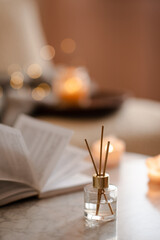 Home liquid fragrance in glass bottle and bamboo sticks over paper book on marble table in living...