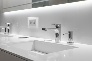 Close-up of two stylish sinks with faucets in white bathroom with a bevelled mirror and backlight. Concept of a modern stylish bathroom for a hotel or spacious home
