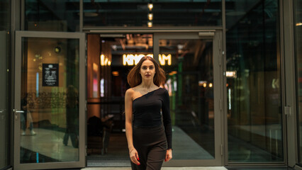Fashionable beautiful woman model in black stylish clothes with trousers and a black one-shoulder top walks in office building