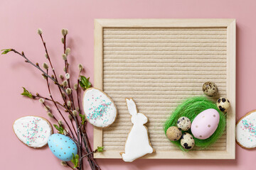 Springtime welcome layout. Letter board, colorful eggs and green branches on a pink background,...