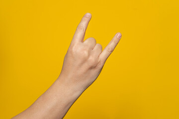 Male hand close-up on a yellow background shows hand gesture. Rock'n'roll. Isolate