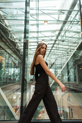 Stylish beautiful successful business woman model in fashion black elegant clothes with a top and pants walking in a glass office building