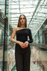 Elegant beautiful young woman model in black stylish clothes with a fashion top and trousers near a glass wall in a business building