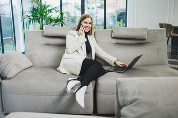 Obraz premium Cute young freelancer woman in casual clothes relaxing on sofa while working on internet via netbook while remote working on project at home.