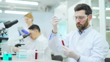 Medical researcher scientist asian man with protection holding blood sample HIV or bacteria testing in test tube and make experiment with colleagues at microbiology biochemistry hematology laboratory
