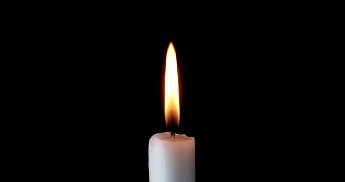 A single white candle burning. Isolated candle burning with dark background. White paraffin candle with yellow shades burns on a black background. Background of remembrance or celebration.