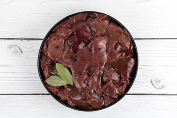 Raw chicken liver on a black plate with spice on a white wooden background. Top view. Copy space. Noise to tail concept.