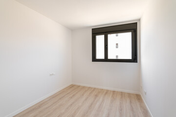 Small empty room without furniture. The floor is new light wood laminate. A window made of black plastic for airing the room. Daylight enters through the frosted glass in the window.