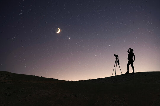 Silhouette of a photographer with camera standing on the hill and looking at the  moon.