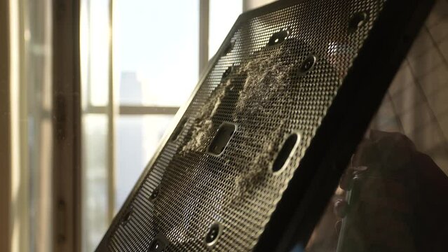 Closeup cropped shot of unrecognizable man cleaning dust off side of computer system case with fan using compressed air spray at desk on background of window and beautiful sunlight at home, slowmotion